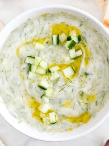 Tzatziki en un bol con pepino, eneldo y aceite de oliva, acompañado de pan de pita.