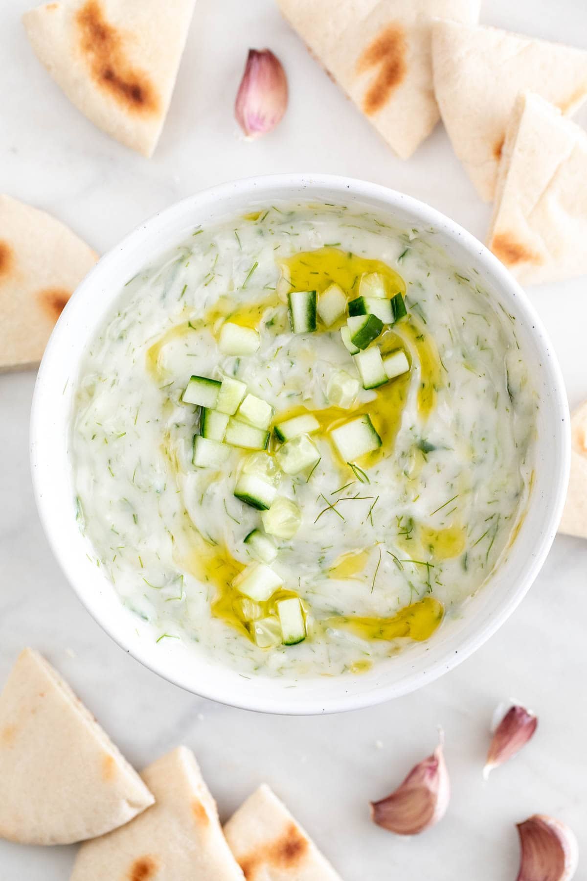 Tzatziki en un bol con pepino, eneldo y aceite de oliva, rodeado de pan de pita.