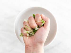 Mano estrujando el pepino sobre un bol.