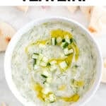 Tzatziki en bol decorado con pepino, aceite de oliva y eneldo con pan pita alrededor.