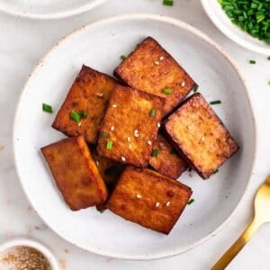 Tofu ahumado decorado con sésamo y cebollino en un plato.