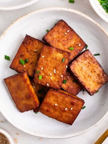 Tofu ahumado decorado con sésamo y cebollino en un plato.