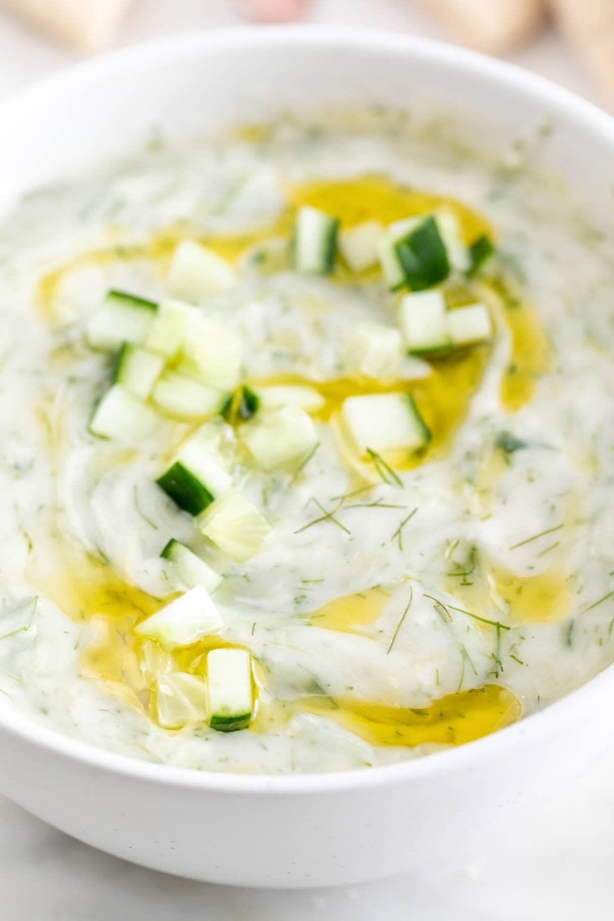 Salsa tzatziki en un bol decorada con pepino, eneldo fresco y aceite de oliva.