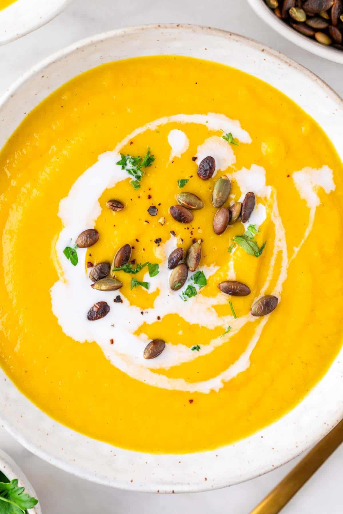 Bol de crema de verduras decorado con leche de coco, perejil y semillas de calabaza.