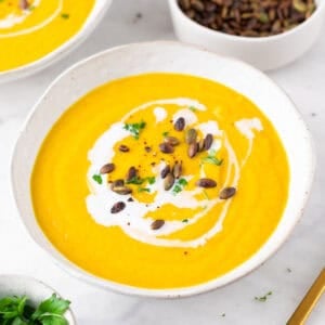 Crema de verduras en un bol, decorada con un chorrito de leche de coco, perejil y semillas de calabaza.