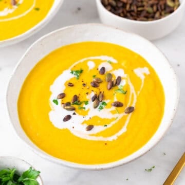 Crema de verduras en un bol, decorada con un chorrito de leche de coco, perejil y semillas de calabaza.