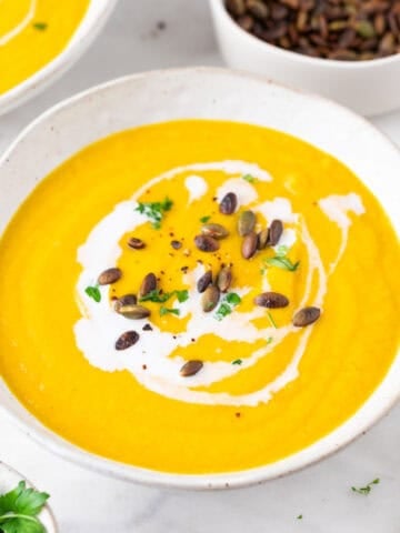 Crema de verduras en un bol, decorada con un chorrito de leche de coco, perejil y semillas de calabaza.