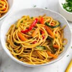 Espaguetis con verduras servidos en un bol, decorados con sésamo y cebollino.