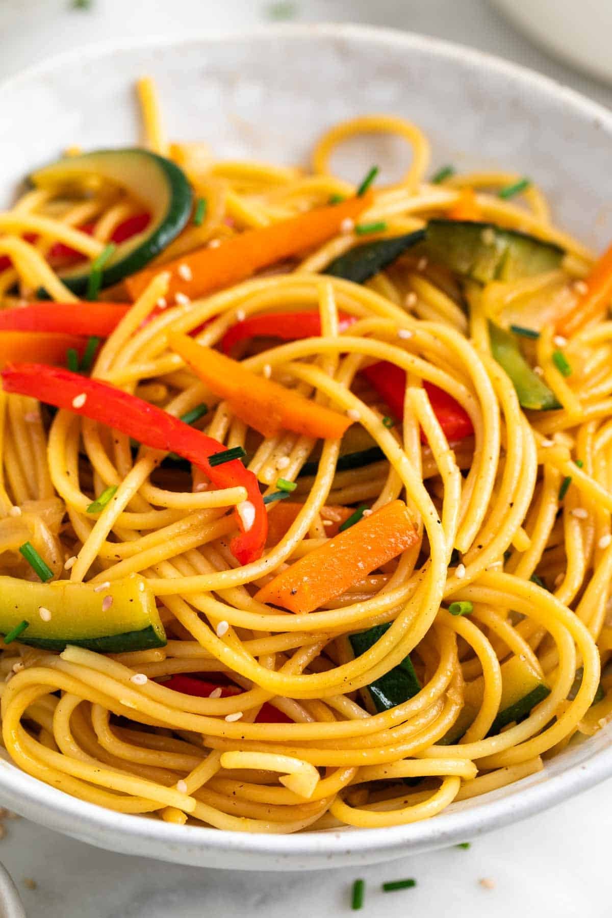 Espaguetis con verduras en un bol decorados con sésamo y cebollino.