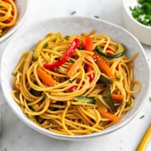 Espaguetis con verduras servidos en un bol, decorados con sésamo y cebollino.