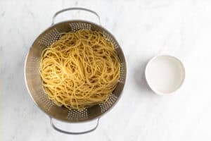 Espaguetis cocinados en un colador y cuenco con agua de cocción.