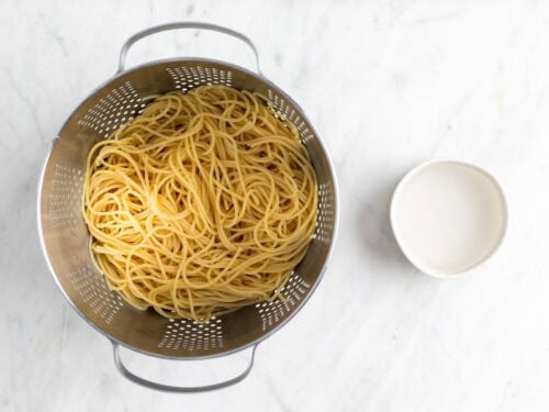 Espaguetis cocinados en un colador y cuenco con agua de cocción.