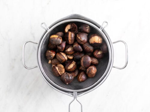 Castañas cocidas en un colador sobre un bol.