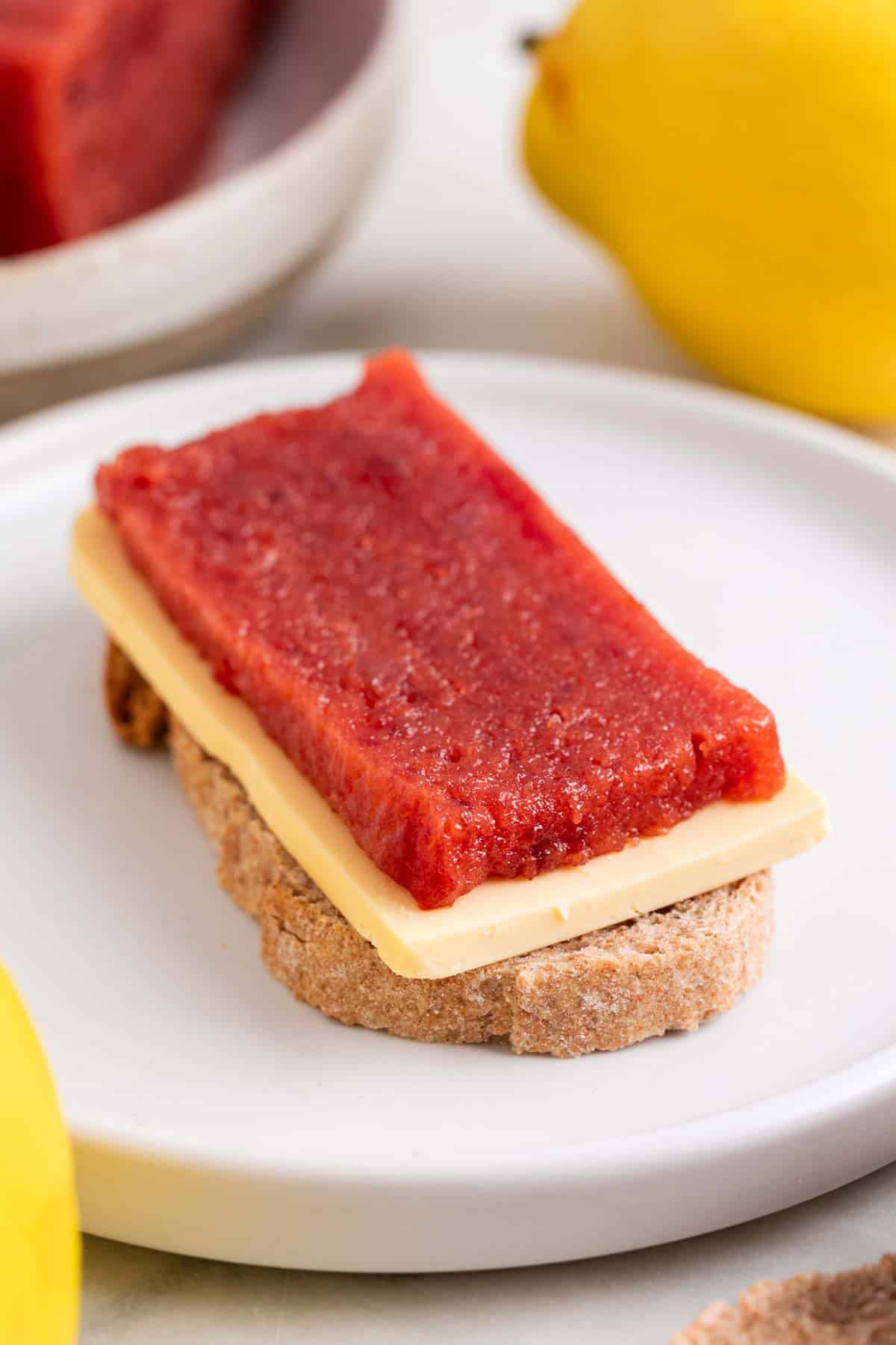 Trozo de pan con queso y dulce de membrillo en un plato.
