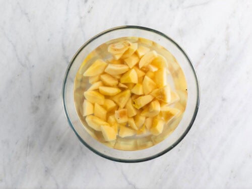 Membrillos pelados y troceados en un bol con agua.
