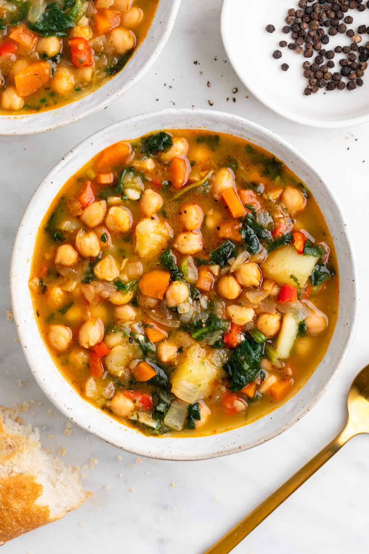 Potaje de garbanzos con verduras con pan y cuchara al lado.