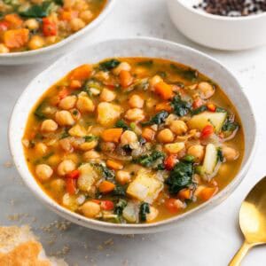 Cuenco de potaje de garbanzos con verduras con pan y cuchara.