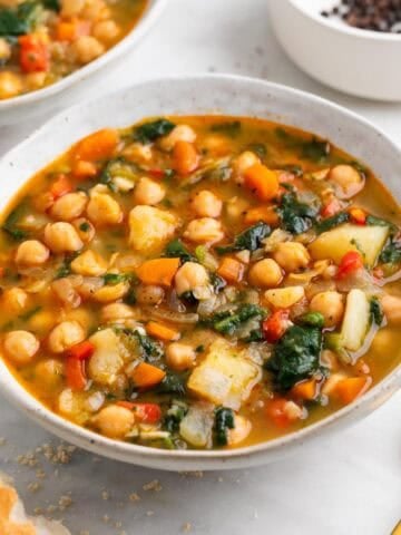 Cuenco de potaje de garbanzos con verduras con pan y cuchara.