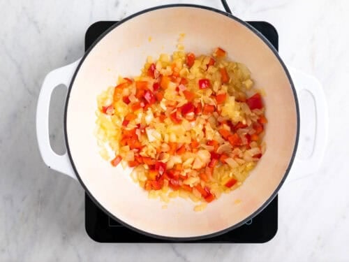 Cebolla, ajo y pimiento rojo salteados en una olla.