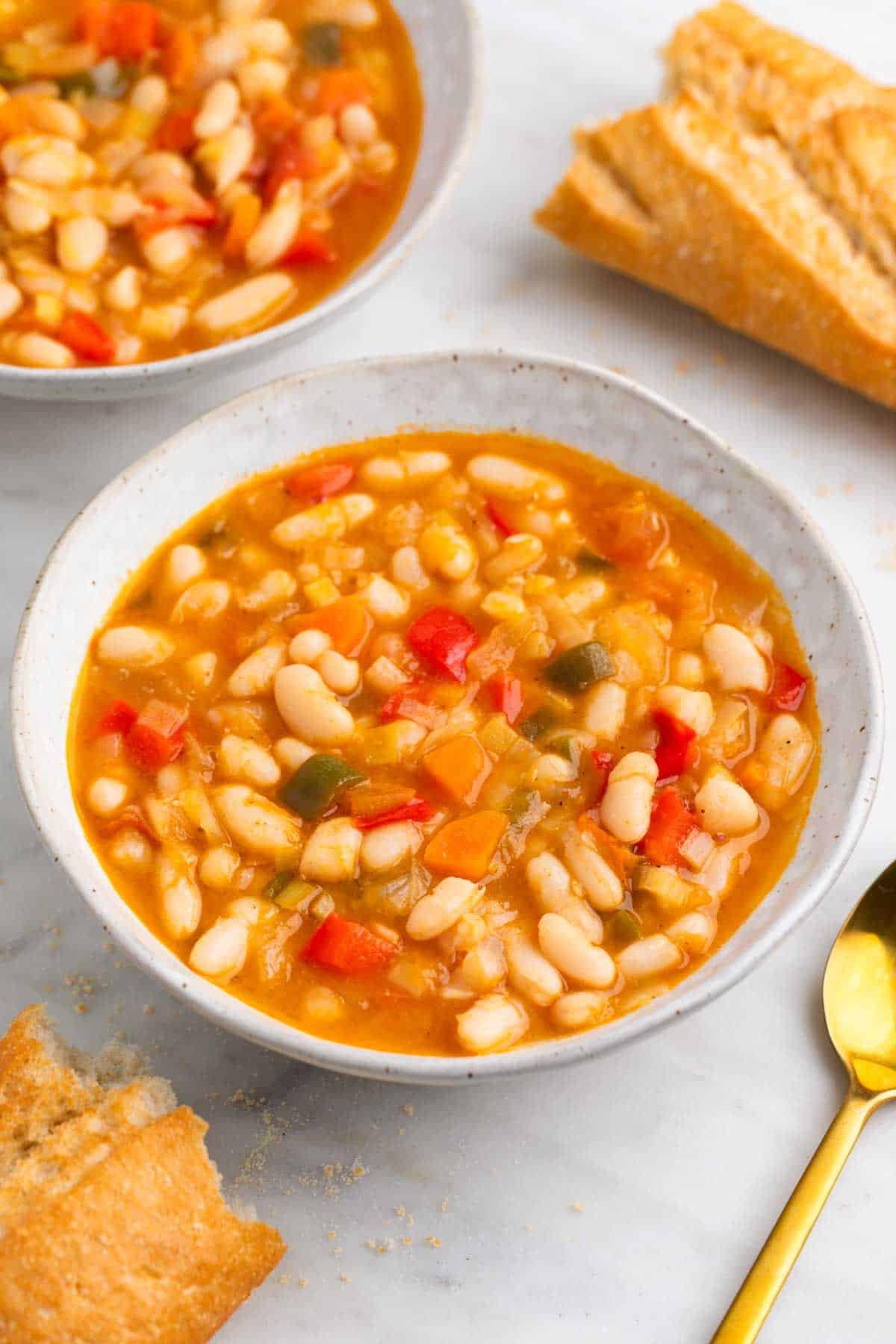 Platos de alubias blancas con verduras servidas con pan.