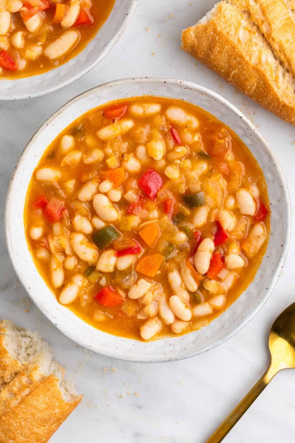 Alubias blancas con verduras en plato hondo acompañadas de pan y cuchara.