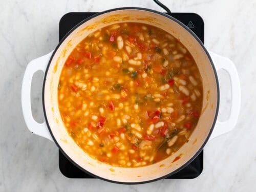 Guiso de alubias blancas con verduras en una olla.