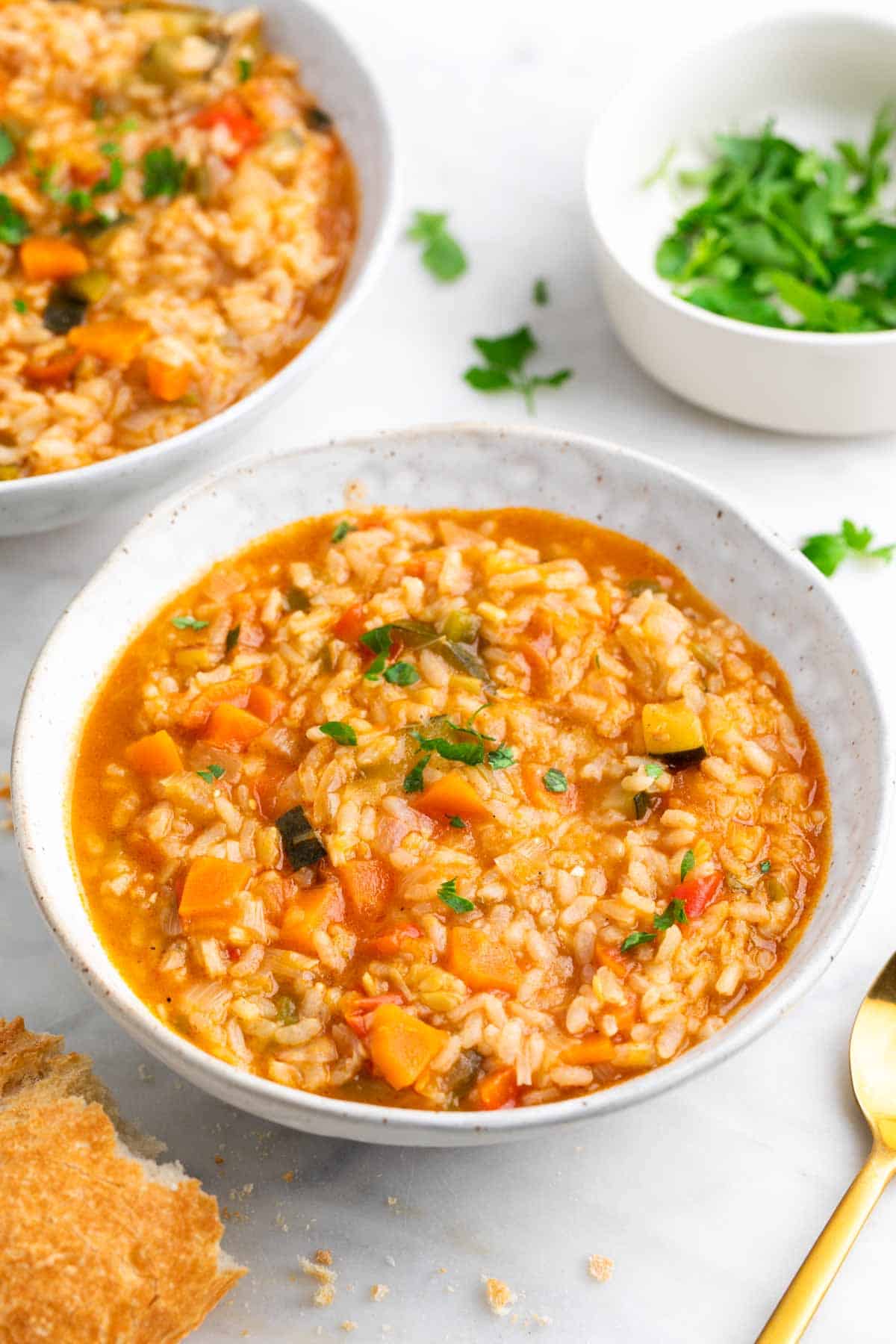 Platos de arroz caldoso con verduras con pan, perejil y un tenedor alrededor.
