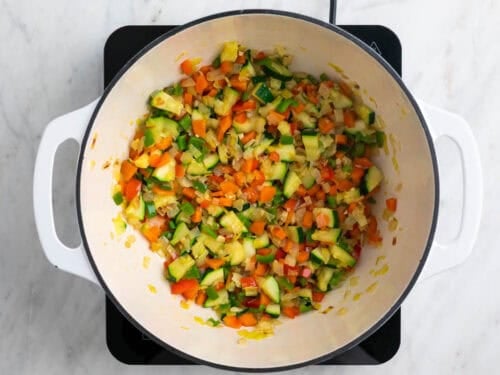 Ajo, cebolla, puerro, zanahoria, pimiento y calabacín salteados en una olla.