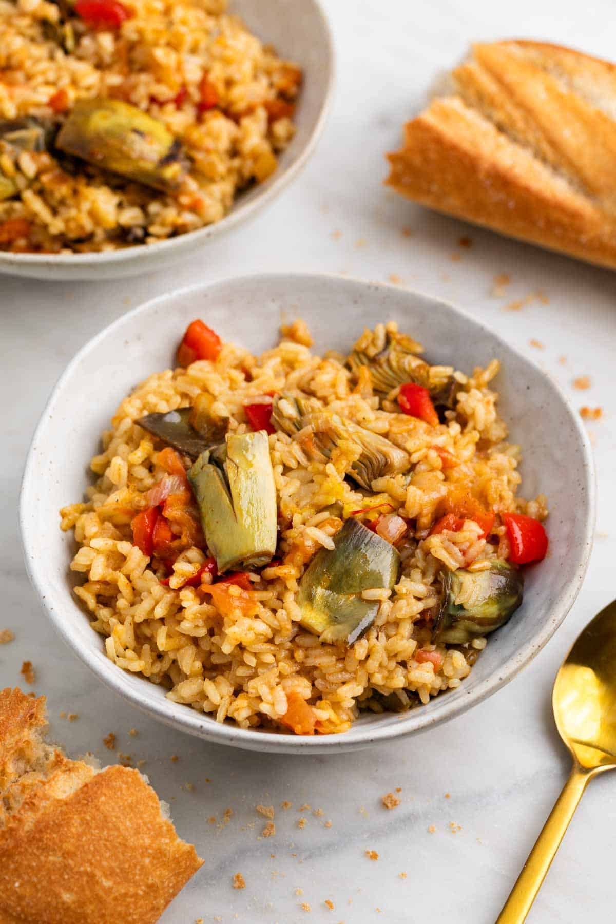 Arroz seco con alcachofas servido en bol con cuchara y pan.