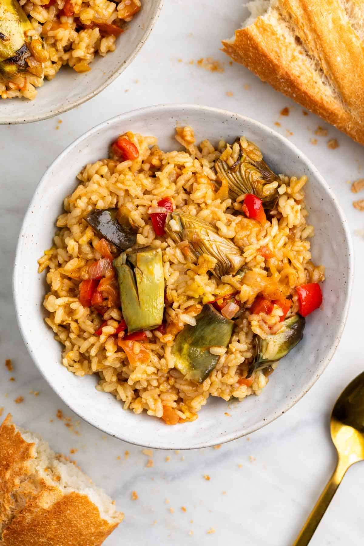 Dos raciones de arroz con alcachofas listas para servir con pan.