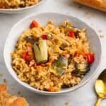 Plato de arroz con alcachofas en bol blanco con pan al lado.