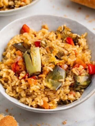 Plato de arroz con alcachofas en bol blanco con pan al lado.