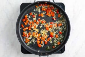 Cebolla y pimiento rojo salteados en una sartén.