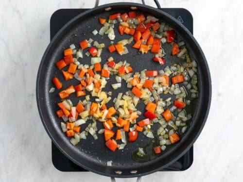 Cebolla y pimiento rojo salteados en una sartén.