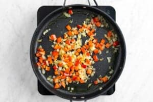 Cebolla, pimiento rojo y ajo salteados en una sartén.