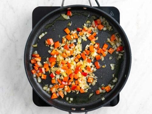 Cebolla, pimiento rojo y ajo salteados en una sartén.