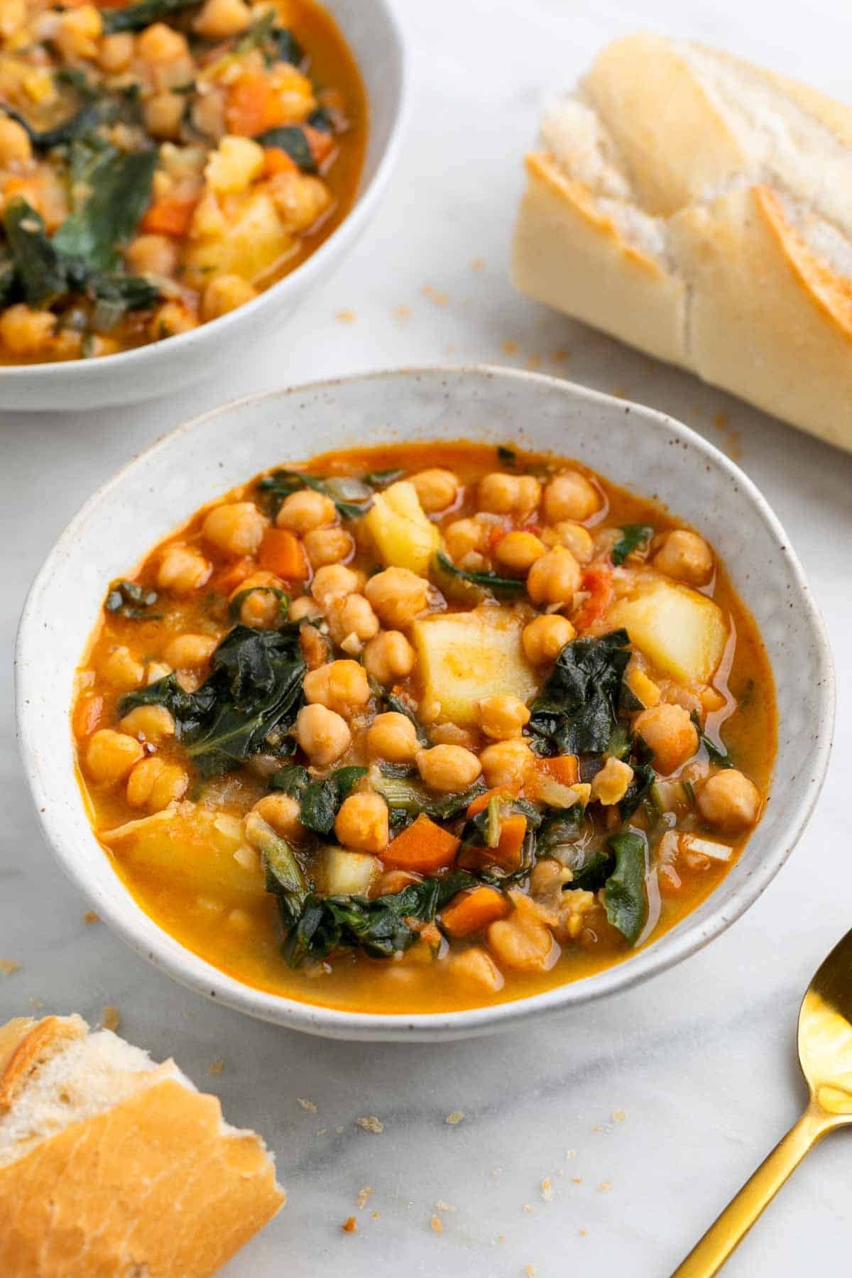 Garbanzos con acelgas servidos en dos boles con pan y una cuchara.