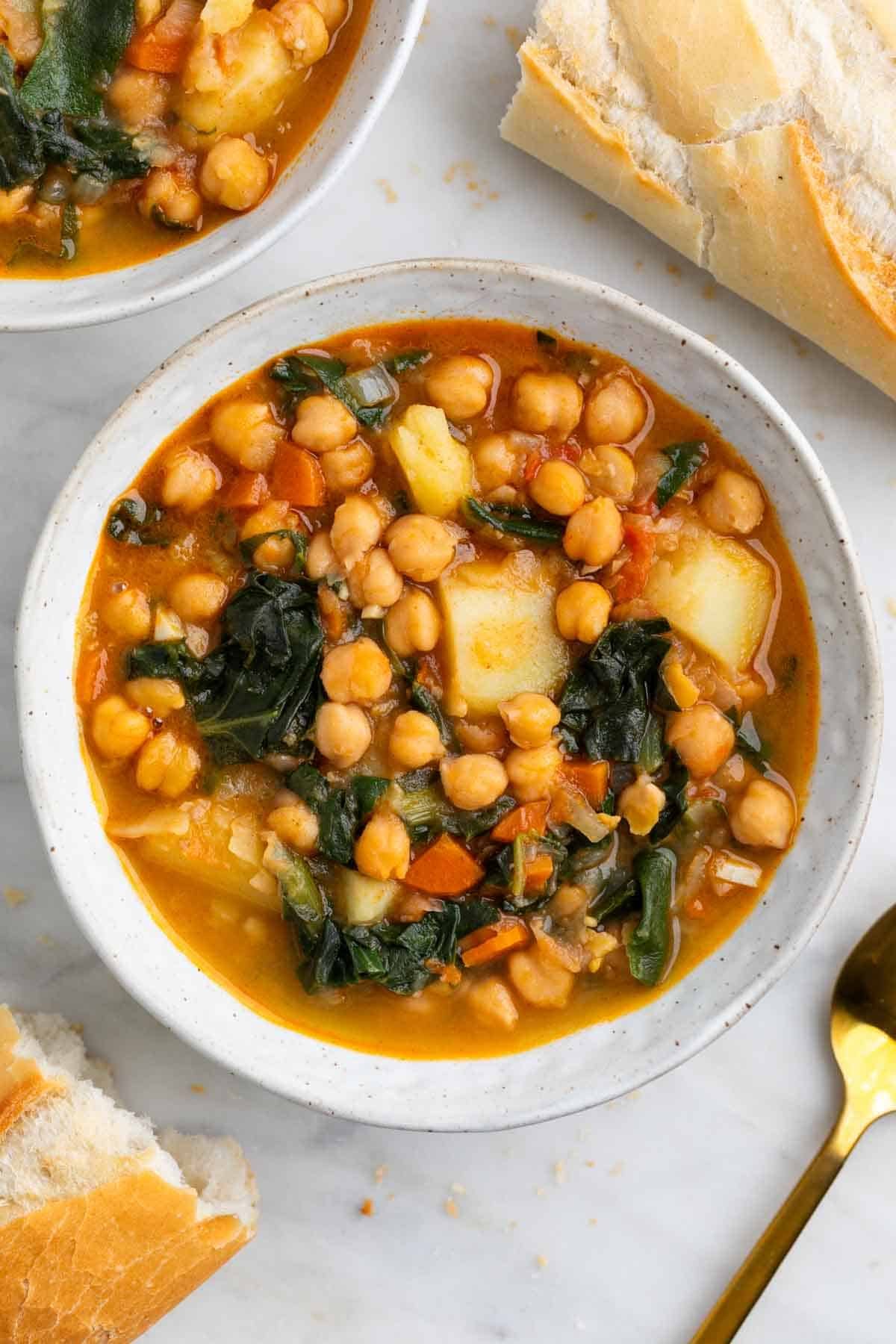 Potaje de garbanzos con acelgas en boles acompañado de pan y cuchara.
