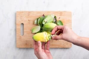 Manos sujetando una alcachofa sin hojas sobre una tabla.