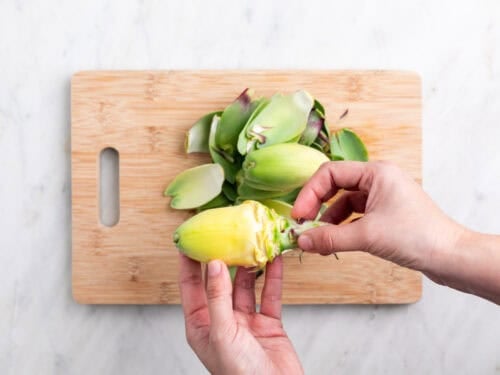 Manos sujetando una alcachofa sin hojas sobre una tabla.
