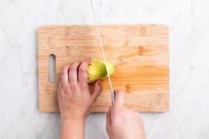 Manos troceado la punta de una alcachofa sin hojas con un cuchillo sobre una tabla.