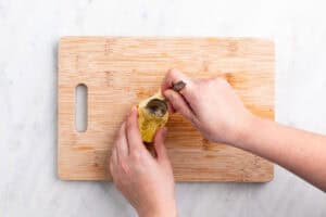 Mano limpiando los pelillos de una alcachofa con una cuchara sobre una tabla.