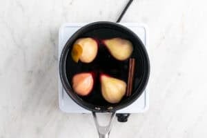 Peras en un cazo con el vino, el azúcar, la canela y la piel de limón.