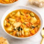 Potaje de verduras en un bol con una cuchara y trozos de pan.