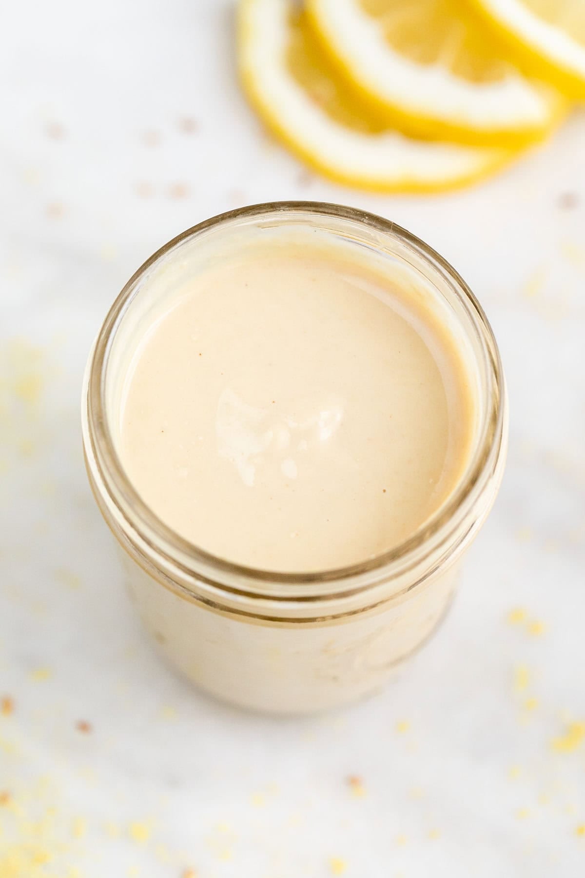 Aliño de tahini en un tarro con rodajas de limón y levadura nutricional alrededor