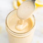Aliño de tahini casero con textura cremosa en un bote, con una cuchara y rodajas de limón