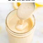 Tarro con aliño de tahini mientras se vierte con una cuchara, acompañado de limón y levadura nutricional