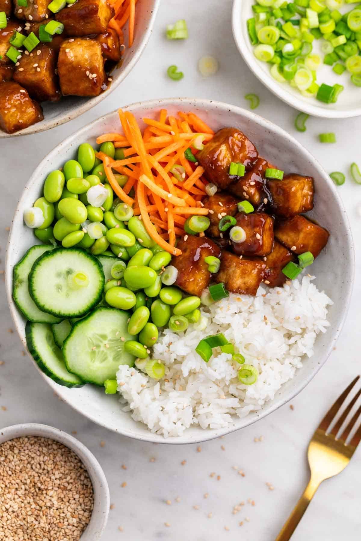 Dos boles de arroz con tofu crujiente, semillas de s&eacute;samo y cebolleta, con un tenedor al lado