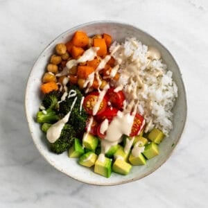 Bol con arroz, verduras asadas, verduras crudas y aliño de tahini por encima