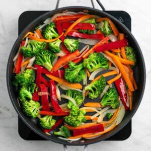 Cebolla, zanahoria, pimiento y brócoli salteados en una sartén.